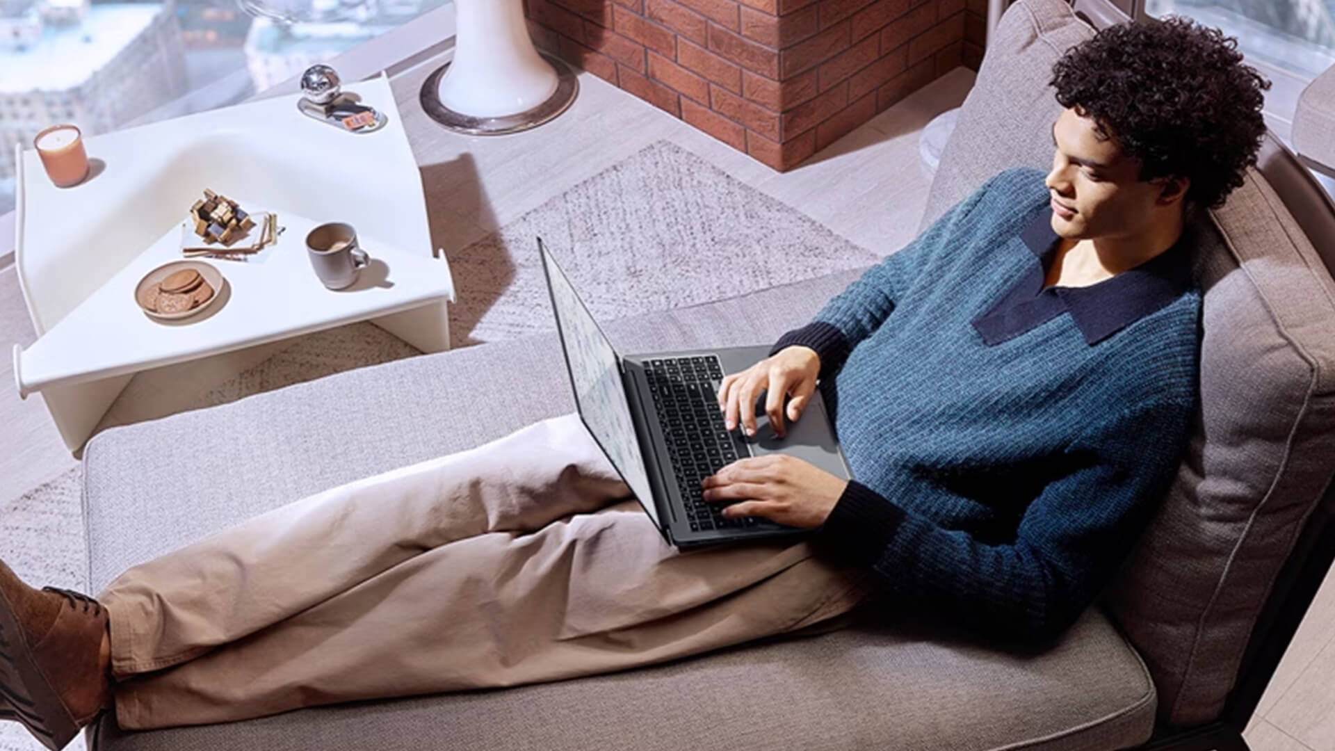 A man relaxing on a sofa while typing on his Samsung laptop.