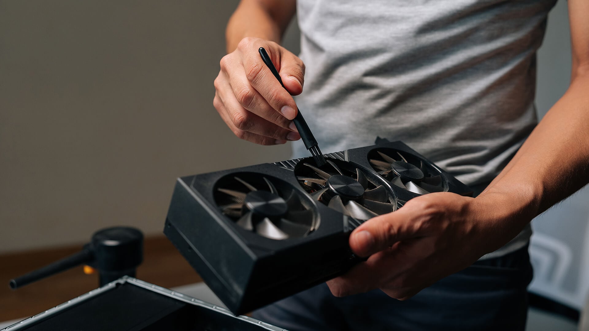 Person cleaning a black three-fan graphics card with a small brush.