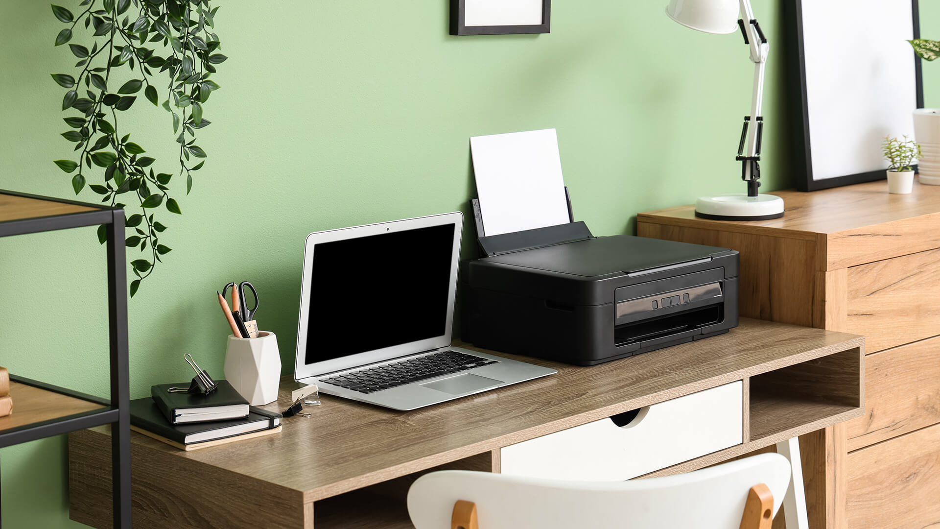 A modern home office desk featuring a laptop and a black laser printer.