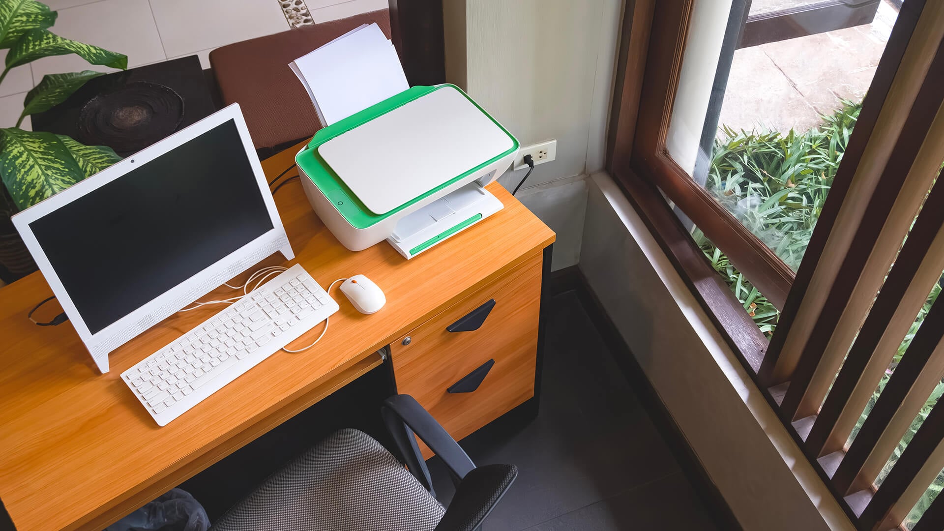 Compact home printer on a desk next to a window and plant.
