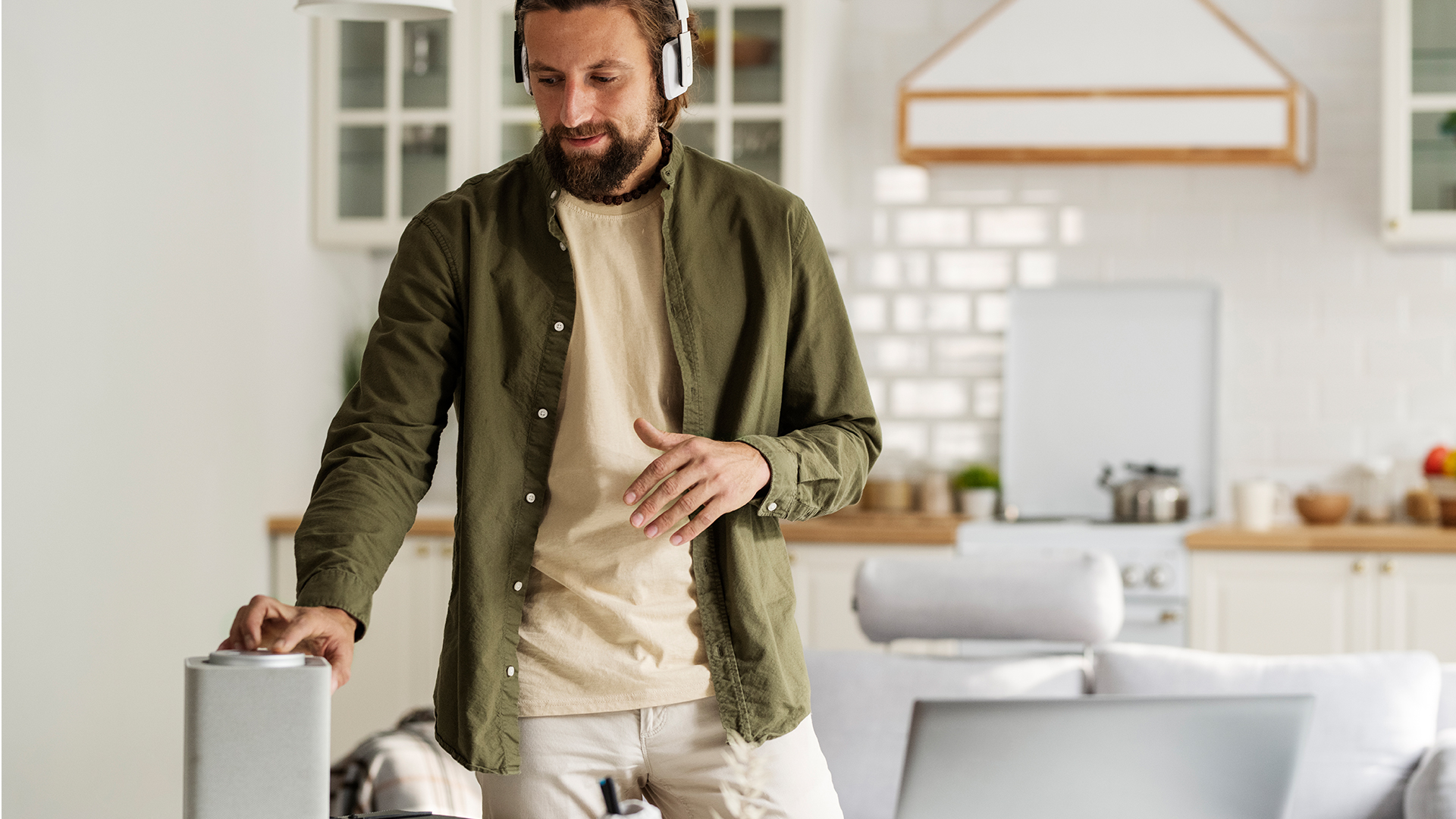 Man with headphones adjusting a wireless speaker in his home.