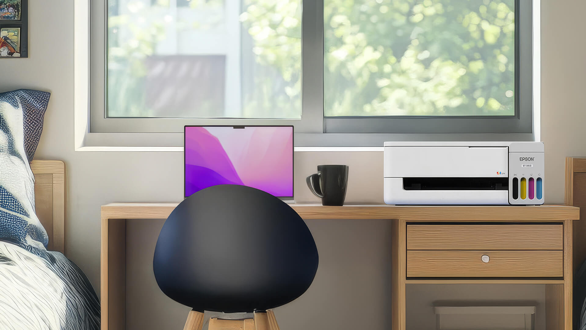 White Epson EcoTank printer sits on a wooden desk next to a laptop in front of a window.