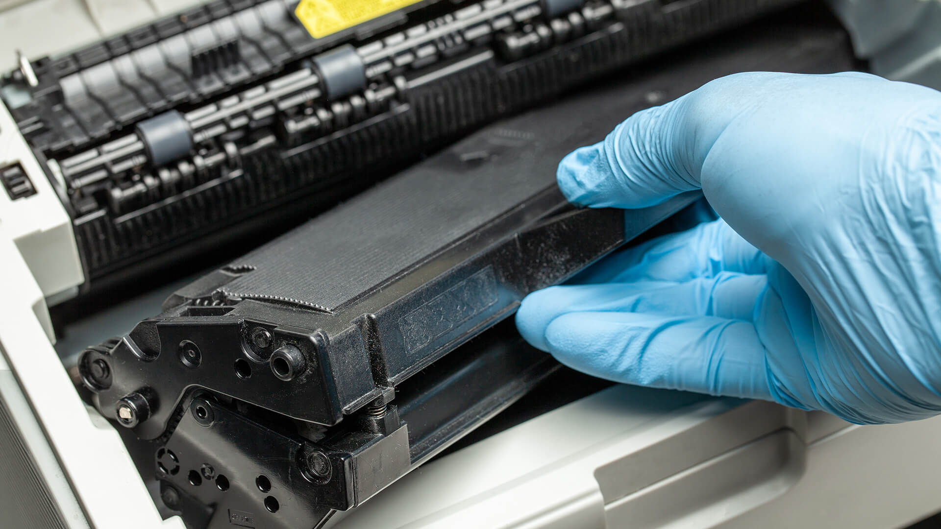 Removing an old Brother printer toner cartridge with blue gloves.