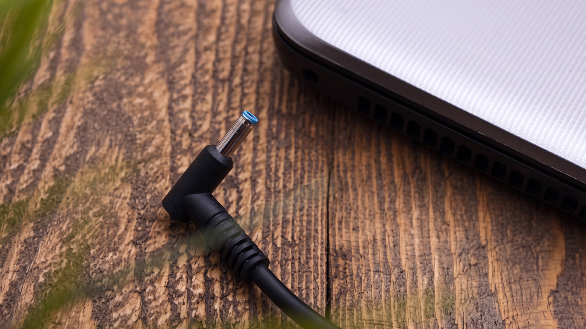 Close-up of a blue-tipped laptop charging cable on a wooden desk.
