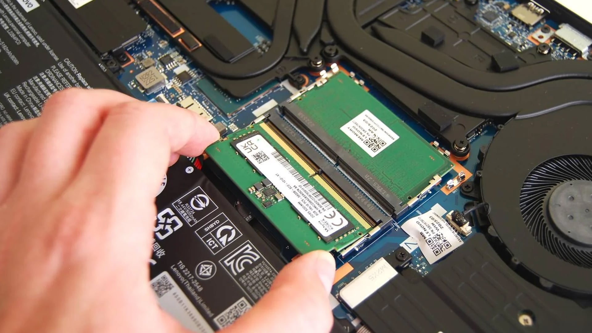 Hand installing a new RAM stick into a laptop motherboard.