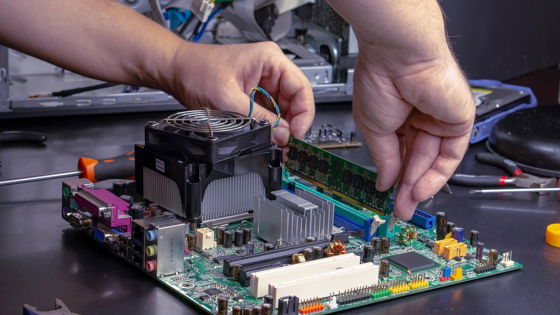 Hands installing a RAM module into the DIMM slot of a motherboard.