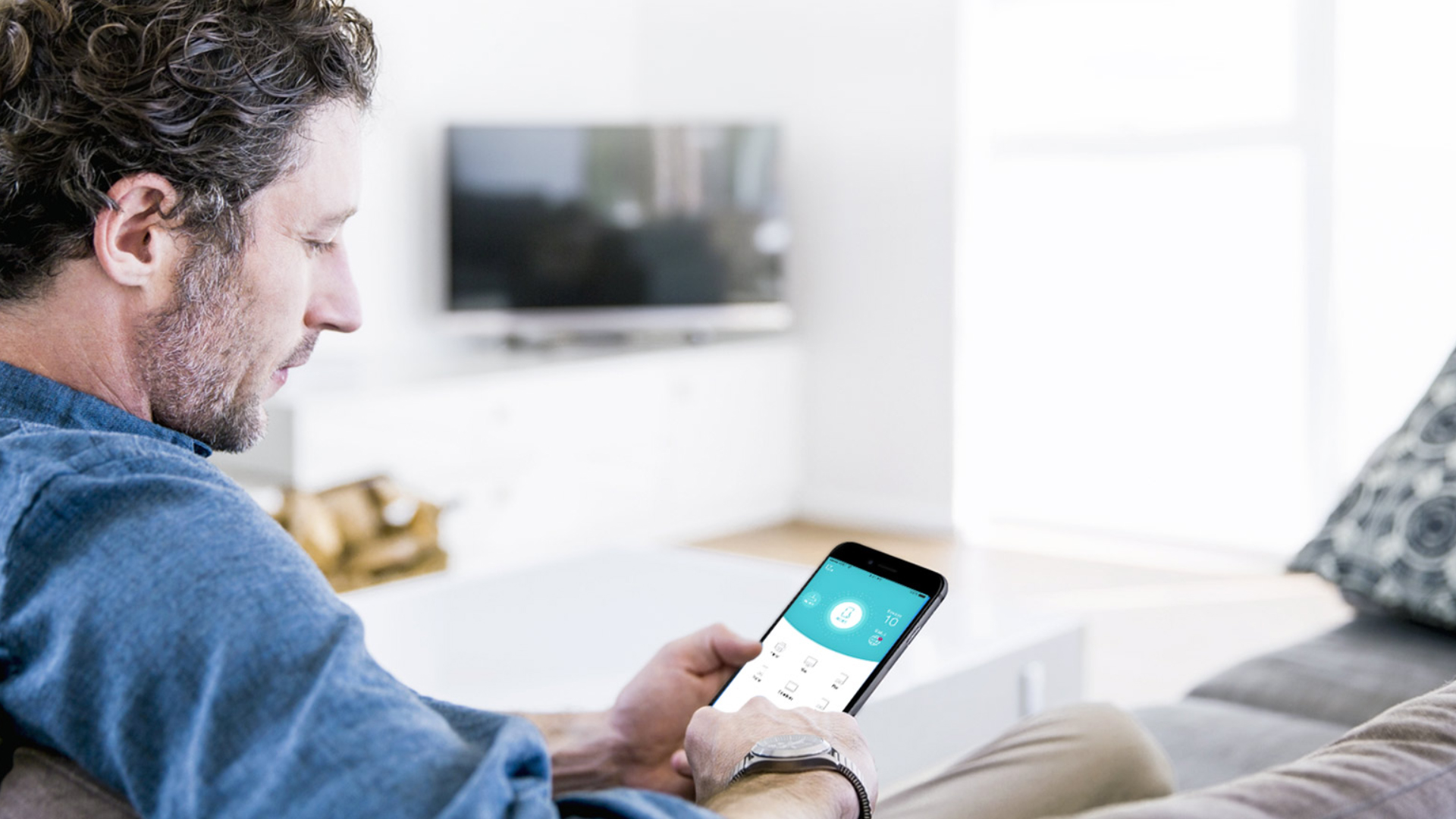 Man holding a smartphone and using the TP-Link Tether mobile app to configure network settings in a living room.