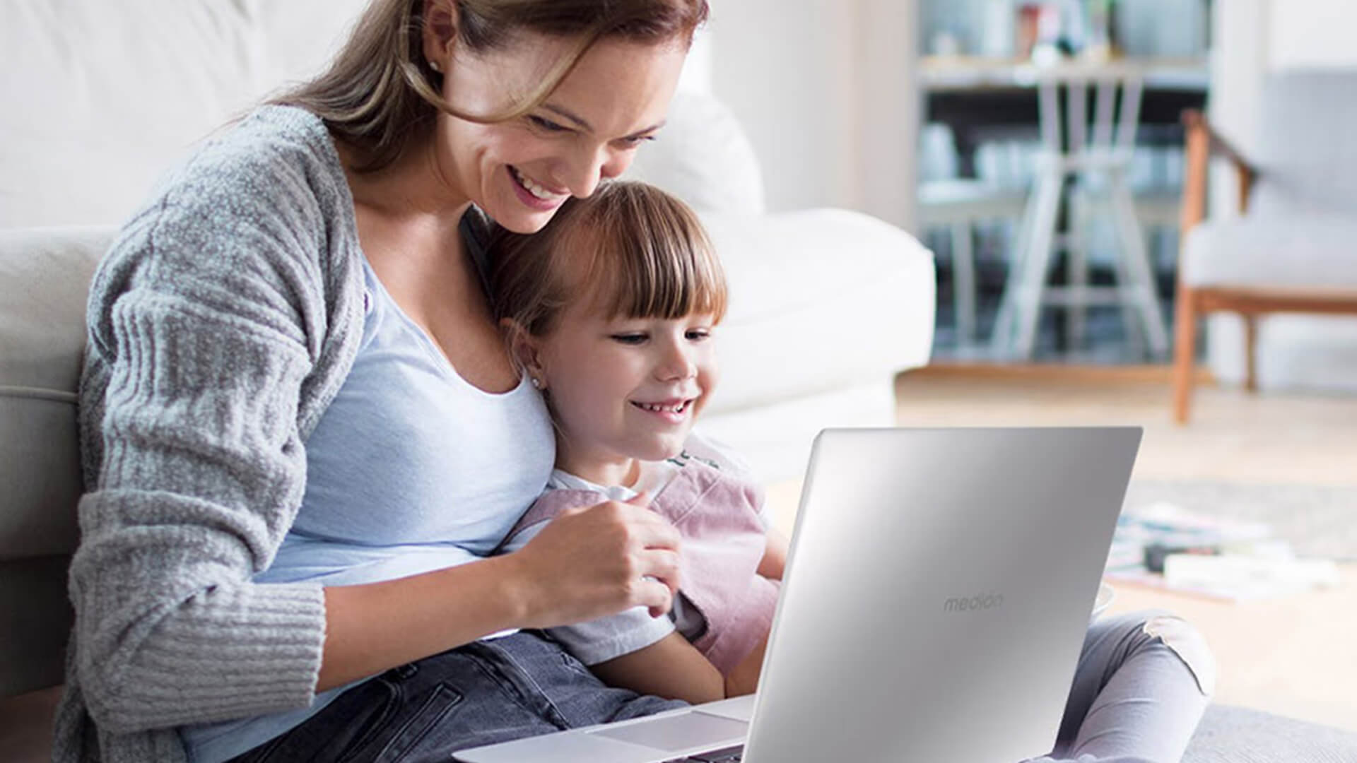 A mother and daughter using a silver Medion laptop together at home.