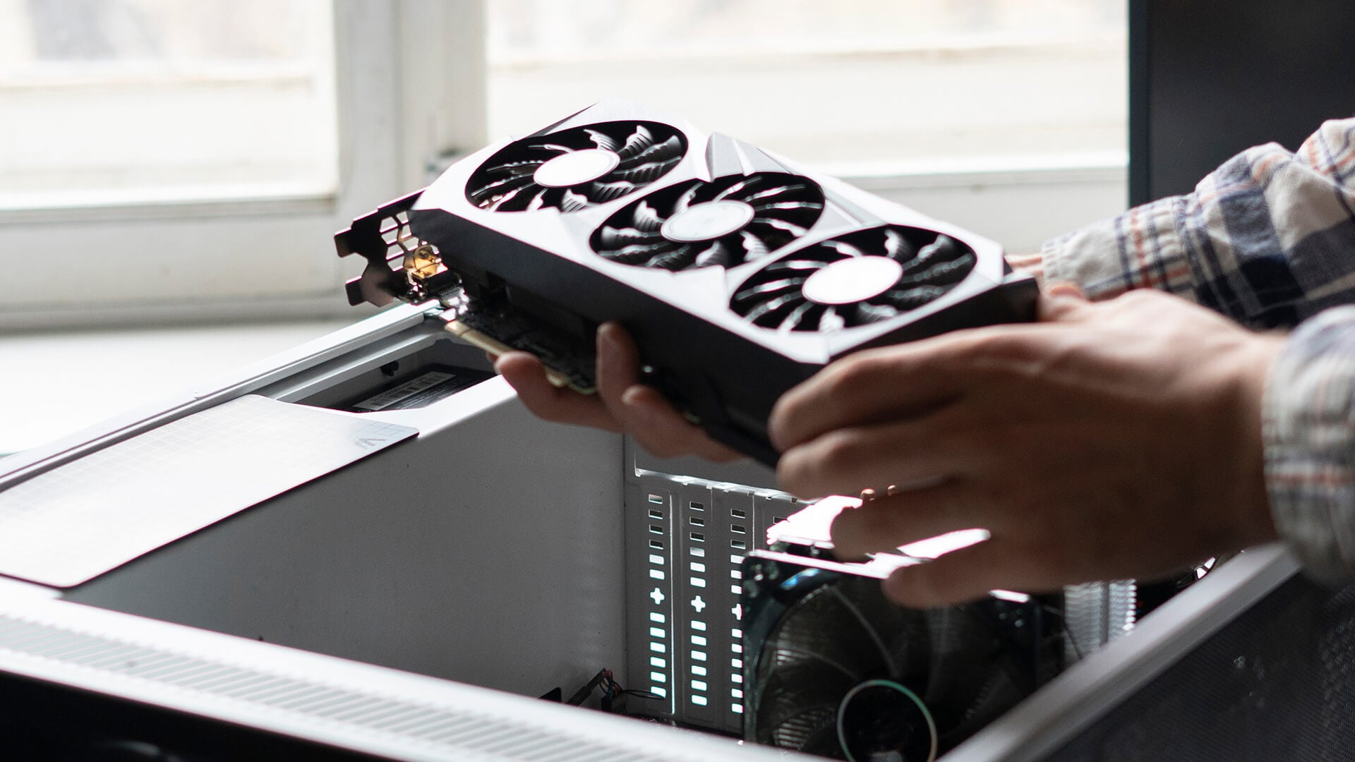 Person holding a triple-fan graphics card to install it into a PC case.