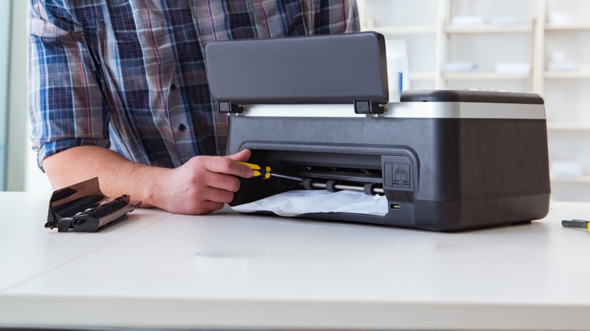 A person using a screwdriver to fix a printer paper jam.