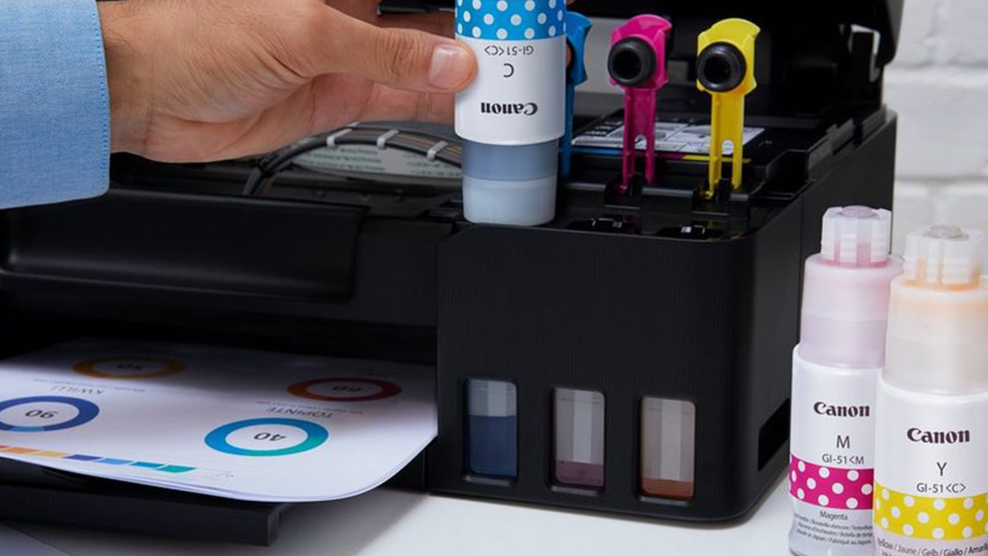 Hand refilling a Canon MegaTank printer with ink bottle.