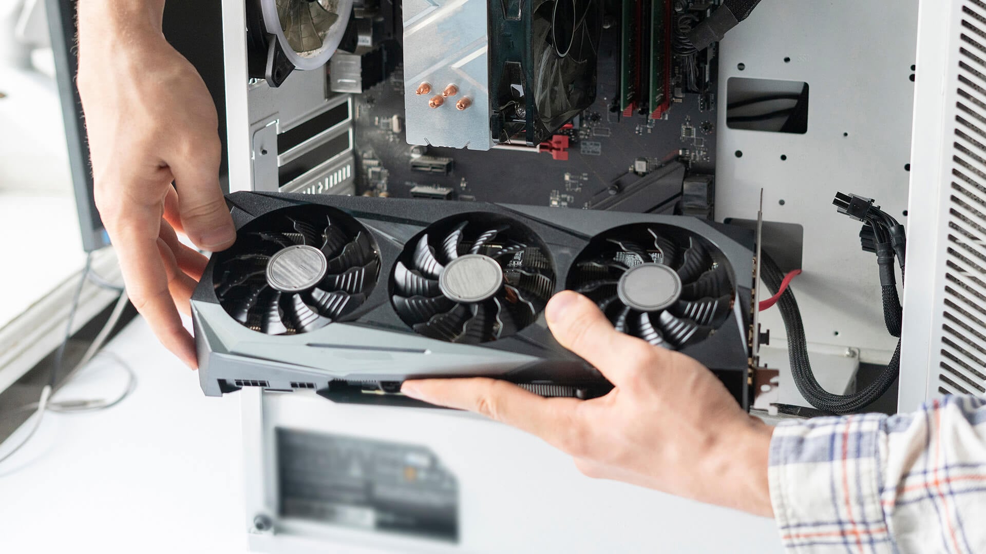 Hands safely removing a large graphics card from a white desktop PC case.
