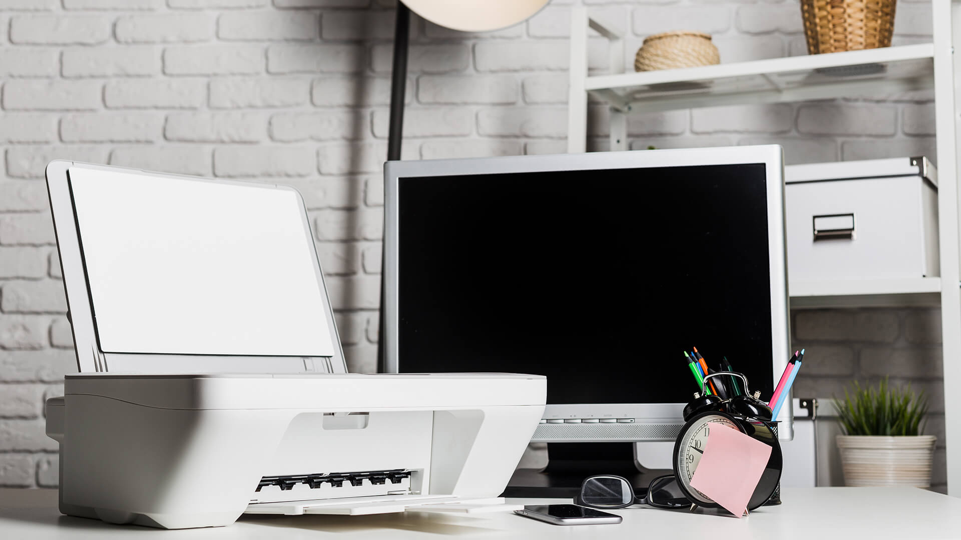 Small home inkjet printer on a desk with a clock and pens.
