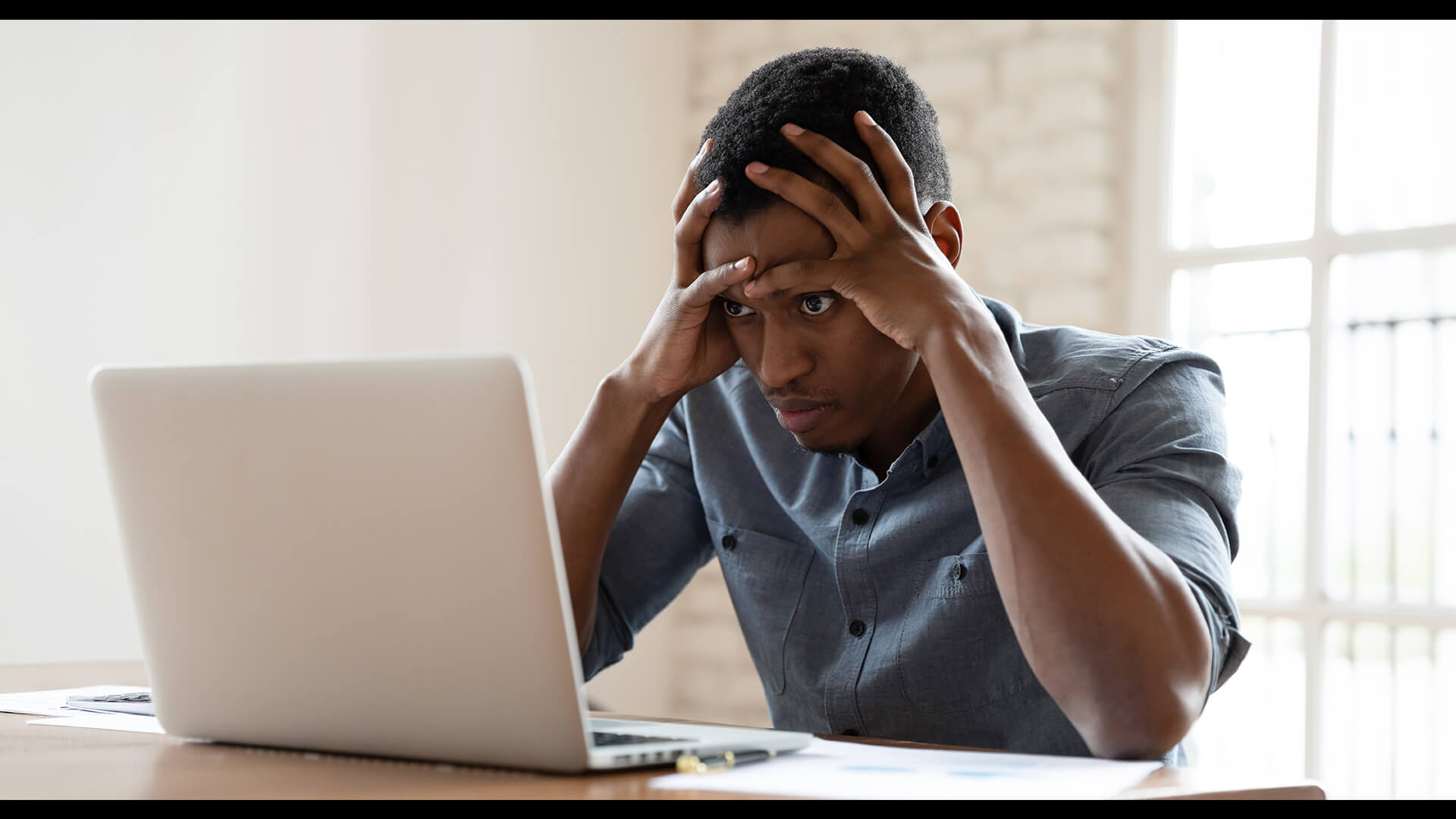 A man looking stressed while trying to work on a slow laptop.