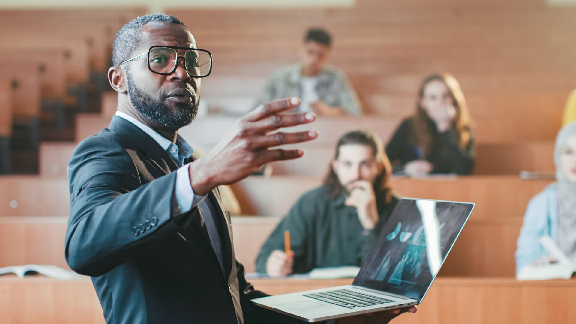 Teacher presenting with a laptop in a lecture hall.