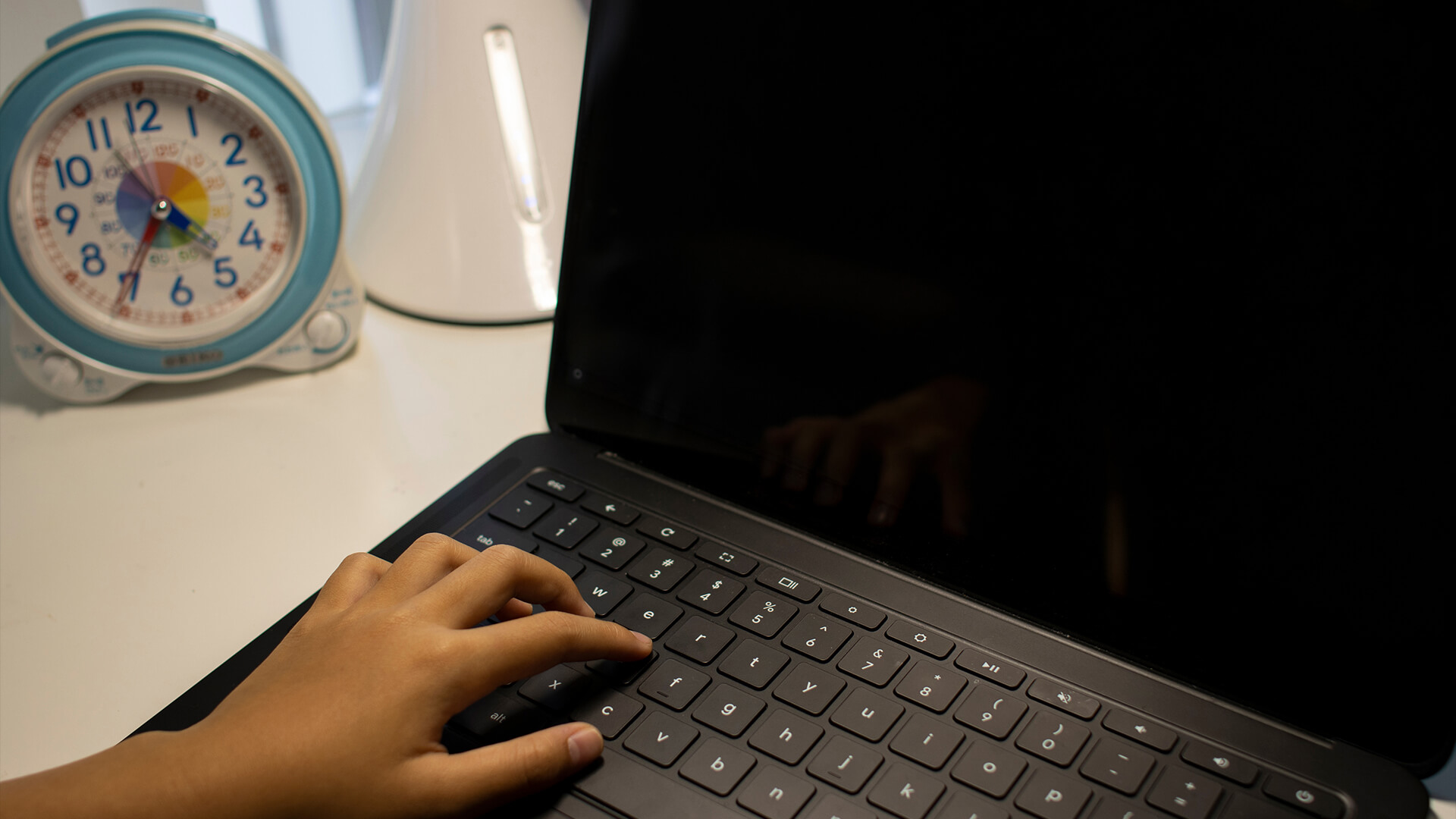 A white Chromebook on a wooden desk next to a window.
