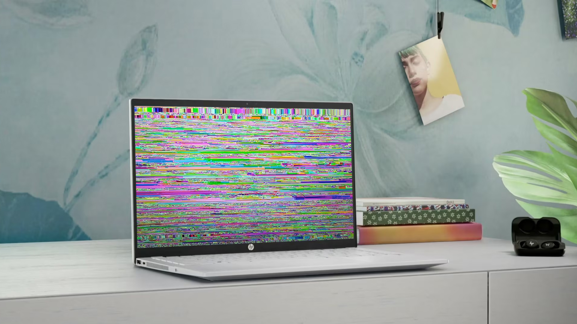 White HP laptop on a desk with a screen displaying colorful horizontal glitch lines.