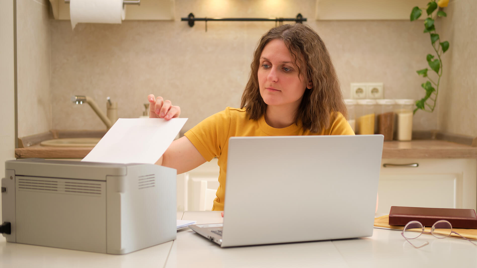 A woman placing paper into a printer next to her laptop.