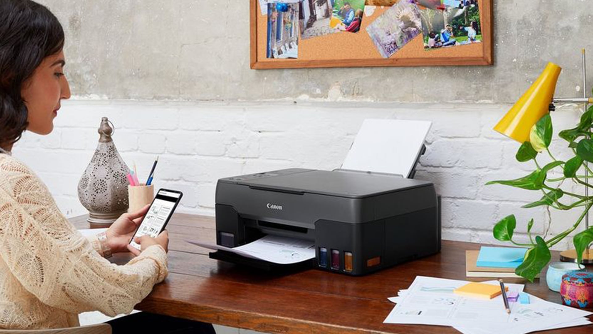 Woman using smartphone next to a Canon MegaTank printer.