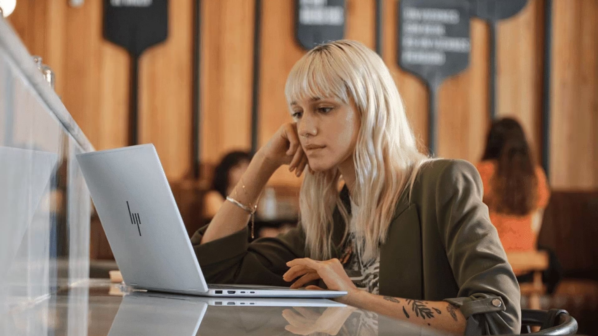 Woman looking intently at a silver HP laptop on a cafe table.